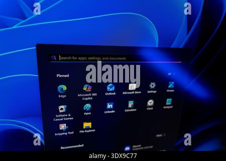 Windows 11 Start menu displaying pinned applications and search bar against a blue abstract background, modern operating system user interface and sof Stock Photo
