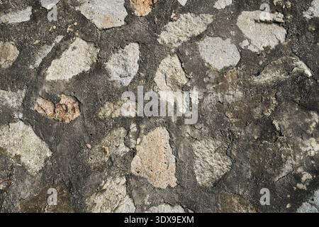 The image captures a rough stone wall with cement filling, emphasizing the detailed textures of the individual stones and the grey cement in between. Stock Photo