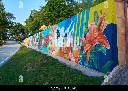 A colorful mural painted on a roadside wall, featuring bright flowers, human figures, and abstract patterns. Stock Photo