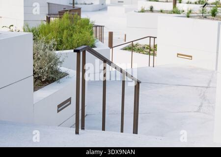 Abstract design of modern urban landscaping featuring minimalist white concrete architecture, pathways, stairs, and green plants Stock Photo