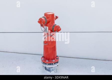Bright red fire hydrant standing against a plain white wall, representing safety, urban infrastructure, and emergency services Stock Photo