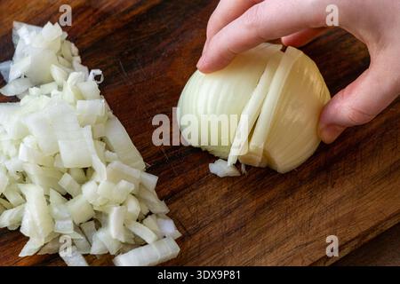 Close up of a hand slicing white onion on a wooden cutting board. Stock Photo