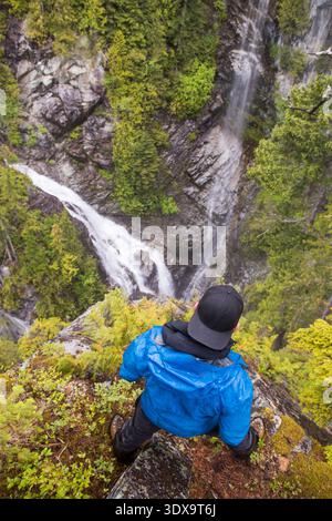 Man stands at the edge of a bluff, looking down on two waterfalls in the Pacific northwest Stock Photo