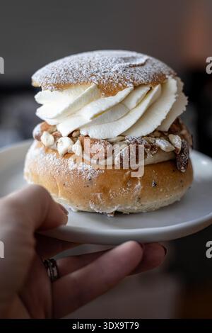 Swedish Semla bun with whipped cream and almonds served by a hand on a white plate Stock Photo