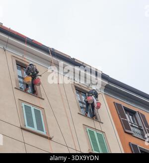 Milan Italy 27 February 2026: Two specialized workers work on a rope suspended along the facade of a building, engaged in maintenance and renovation w Stock Photo