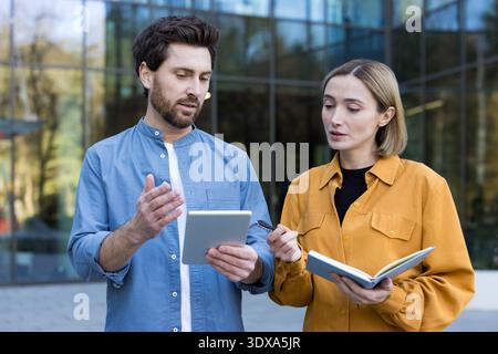 Business professionals collaborating and having a serious discussion outdoors, working on a project with a digital tablet and notebook in front of a modern building Stock Photo
