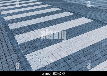 Pedestrian crossing markings creating a rhythmic pattern of white and blue stripes on a textured paved street surface Stock Photo
