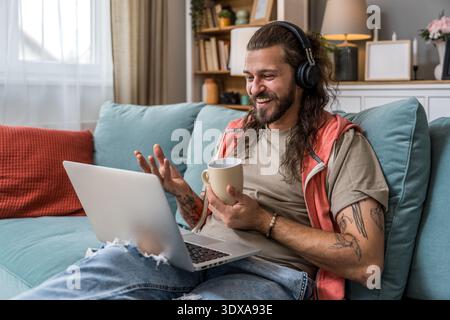 Freelance AI expert working remotely, sipping coffee while using laptop and headphones, focused on innovation consulting, digital strategy and expat l Stock Photo