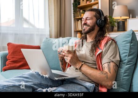 Freelance AI expert working remotely, sipping coffee while using laptop and headphones, focused on innovation consulting, digital strategy and expat l Stock Photo