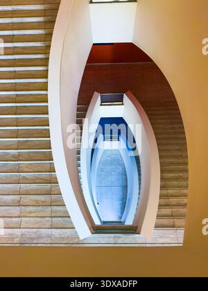 Symmetrical overhead view of modern spiral staircase, curved white balustrades and marble steps, geometric lines, architectural minimalism. Stock Photo