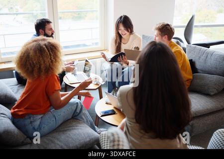 High angle view of smiling young female business expert reading diary while sitting with colleagues in office Stock Photo