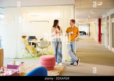 Male and female business experts having coffee while talking with each other standing in office lobby Stock Photo