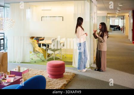 Full length of female business colleagues talking with each other while standing in office lobby Stock Photo