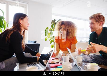 Smiling young female entrepreneur discussing ideas with colleagues in coworking office Stock Photo