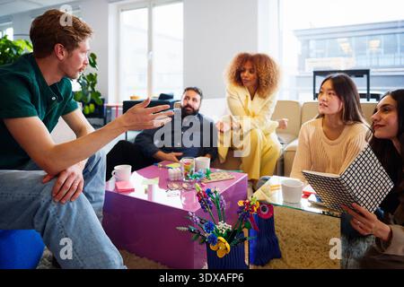 Businessman sharing ideas with colleagues sitting in office lobby Stock Photo