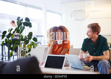 Smiling curly haired businesswoman taking coffee break with male colleague in office lobby Stock Photo