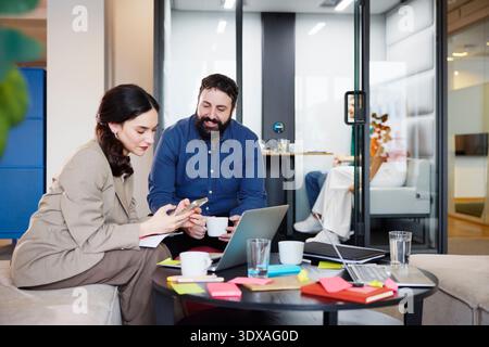 Smiling businessman sitting with female colleague using smart phone in office Stock Photo