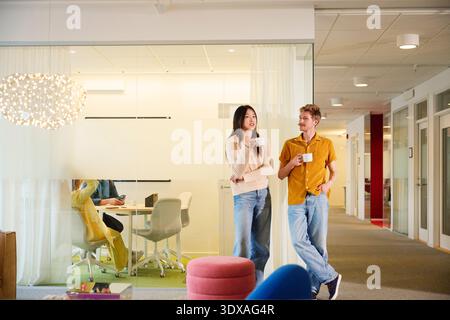 Male and female business professionals having coffee while talking with each other standing in office lobby Stock Photo