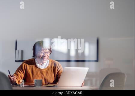 Smiling businesswoman doing video call on laptop while sitting at desk in office Stock Photo