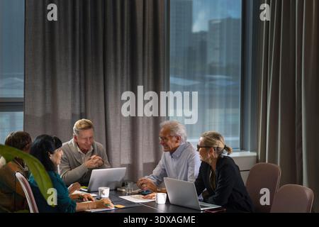 Group of smiling senior business professionals discussing while sitting around table in meeting room Stock Photo