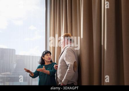 Senior businesswoman gesturing while explaining ideas to male coworker standing near window in office Stock Photo