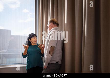 Senior female business entrepreneur gesturing while explaining ideas to male coworker near window in office Stock Photo