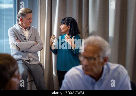 Female business professional discussing with male colleague while standing near curtain of window in office Stock Photo