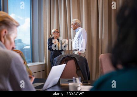 Senior businesswoman communicating with male colleague standing near window in office Stock Photo