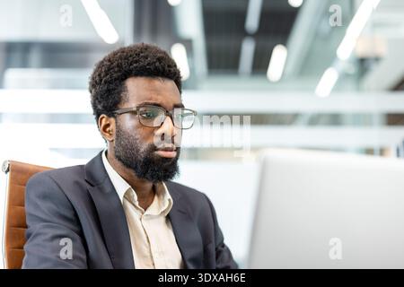 Young ethnic businessman wearing eyeglasses concentrating on his work at the office, using a laptop and demonstrating dedication, professionalism, and commitment to his business tasks Stock Photo