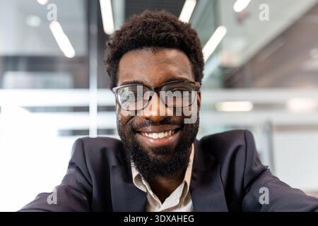 Confident young business professional with an engaging smile and beard wearing a smart suit and glasses, presenting a friendly and approachable corporate image in an office setting Stock Photo