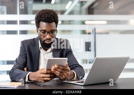 Young professional man working with focus and dedication on a digital tablet at his desk, using modern technology for business tasks in a contemporary office setting Stock Photo