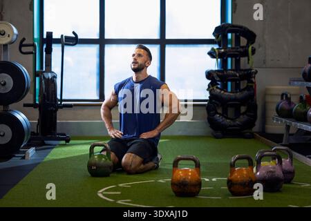 Muscular man with arms akimbo kneeling on floor while working out in gym Stock Photo