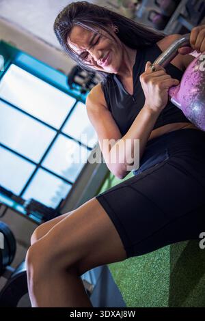 Determined female athlete doing abdominal exercise with kettlebell in gym Stock Photo