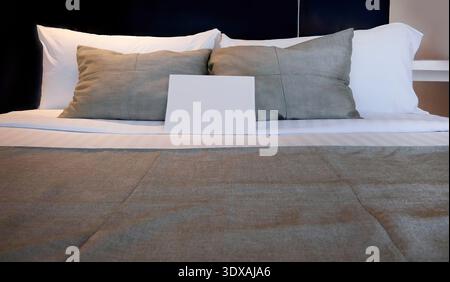 Interior design mockup featuring a blank white paper card standing on soft pillows on a neatly made bed. High-quality background with copy space, perf Stock Photo