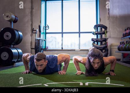 Male and female athletes doing push-ups in gym Stock Photo