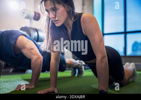 Determined woman doing push-ups next to man in gym Stock Photo