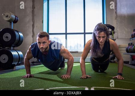 Determined athletes doing push-ups while working out in gym Stock Photo