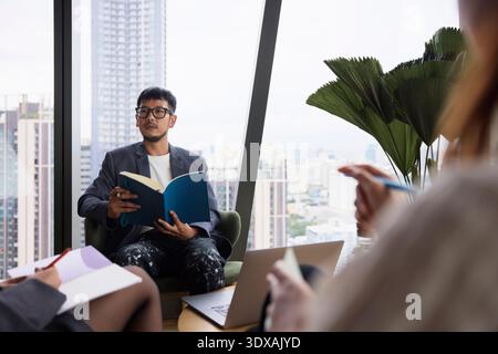 Young male entrepreneur holding book while sitting on chair in office meeting Stock Photo