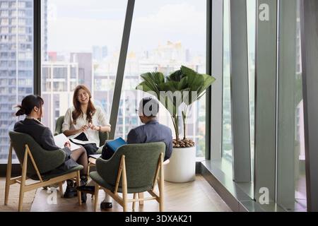 Happy businesswoman sitting with colleagues on chair during office meeting Stock Photo