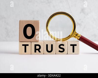 Magnifying glass examining wooden cubes spelling ZERO TRUST, symbolizing zero trust security concept for business information security network. Stock Photo