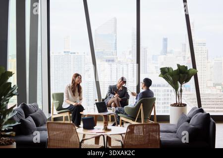 Male manager discussing strategies with female coworkers sitting on chairs at office Stock Photo