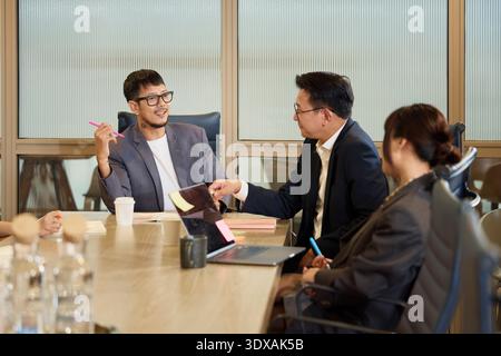 Young male colleague discussing with manager while sitting around table in meeting room Stock Photo