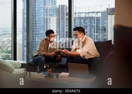 Young businessman listening to manager planning strategies while sitting on sofa Stock Photo