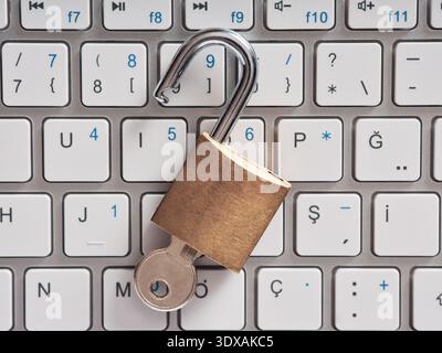 Unlocked padlock with a key resting on a computer keyboard, symbolizing data vulnerability, internet security risks, and privacy threats Stock Photo