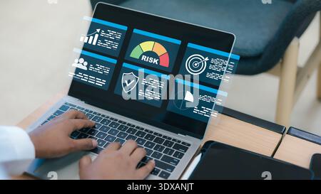Close up of a businessman hands typing on a laptop computer keyboard with virtual holographic risk assessment dashboard and data analytics icons on sc Stock Photo