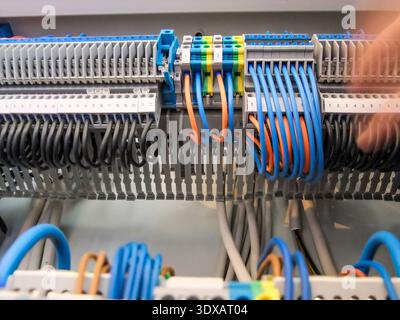 Wiring of an electrical panel shows an organized array of black, blue, and orange wires connected to terminal blocks in a control cabinet. Stock Photo