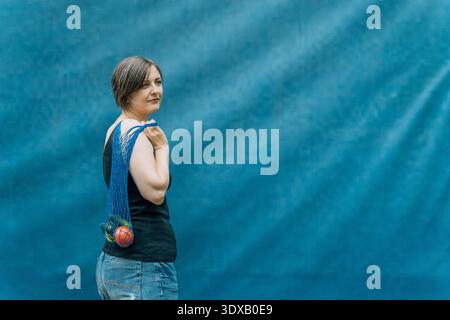 Blonde woman carrying mesh grocery bag over shoulder, back view on blue background Stock Photo