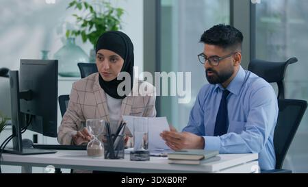 Two business colleagues concentrated in office talking with computer working Arabian businesswoman typing listening Muslim businessman leader boss Stock Photo