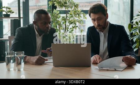 Two diverse business men team upset with bad result businessmen workers multiracial partners in office difficulty trouble with papers and laptop Stock Photo