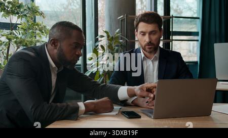 Two diverse multiracial businessmen teamwork in office two men business workers employers discussing online stats result graphics project startup with Stock Photo